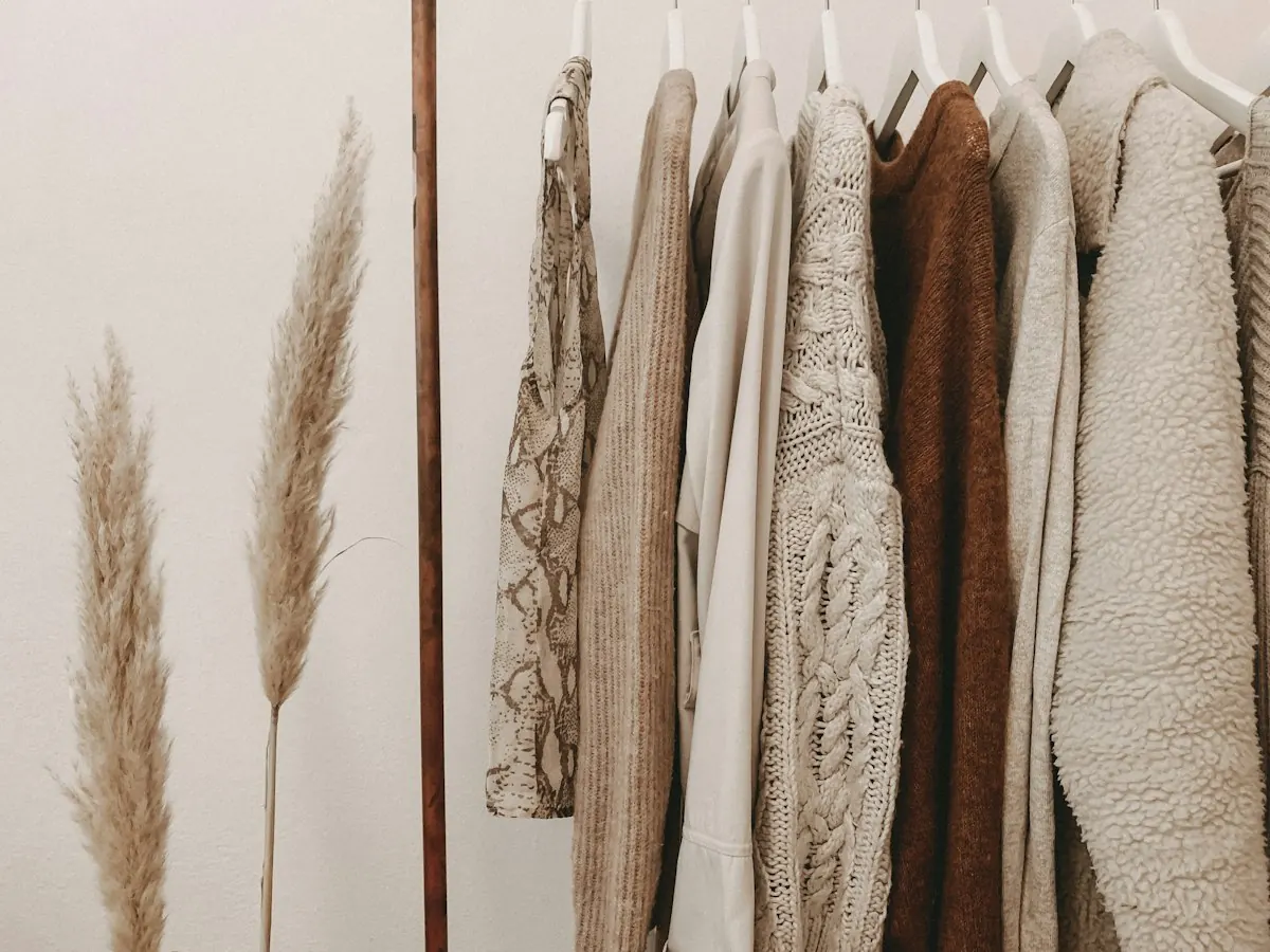 Neutral sweaters hanging neatly beside dried pampas grass